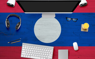 Laos flag background with headphone,computer keyboard and mouse on national office desk table.Top view with copy space.Flat Lay.
