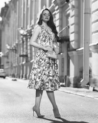 Beautiful brunette young woman wearing stylish sunglasses, colorful green midi dress and high heels standing at city street. Fashion full length portrait. Sunny day