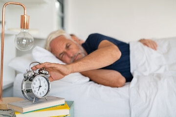 Mature man turning off alarm clock