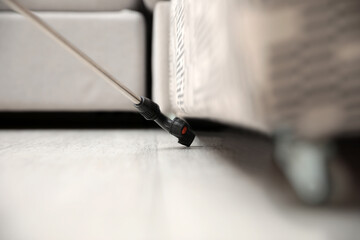 Fototapeta premium Spraying pesticide under furniture indoors, closeup. Pest control service