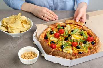 Woman taking slice of delicious vegetable pizza at grey table, closeup