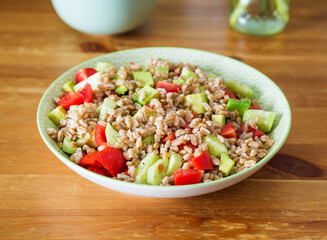Fresh Italian farro spelt salad with tomatoes, avocado and cucumbers on wooden kitchen table. Easy recipe whole food meal - 363808879