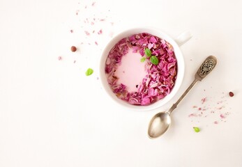 Pink roses milk. Moon milk with rose petals in a white cup on a white background with space for text. Top view