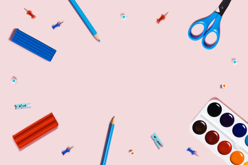 Back to school picture with blue and pencils, red paper clips, scissors, watercolor and plasticine on pink background.