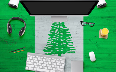Norfolk Island flag background with headphone,computer keyboard and mouse on national office desk table.Top view with copy space.Flat Lay.