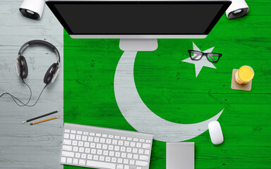 Pakistan flag background with headphone,computer keyboard and mouse on national office desk table.Top view with copy space.Flat Lay.