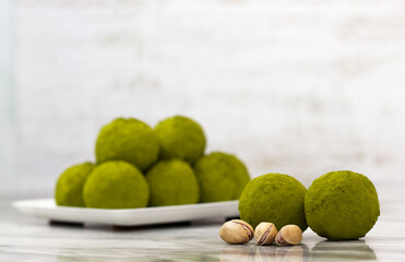 Homemade energy balls with dried apricots, raisins, dates, prunes, walnuts, pistachios and green matcha. Healthy sweet food. Energy balls in a plate on a marble grey background. Close up. Side view.