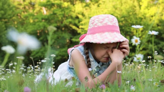 the child sneezes. allergy. sneezing at flowering plants. Cute little girl in summer dress and hat lying on the grass.