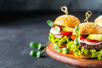 Burgers with meat cutlet, fresh lettuce, tomatoes, onions on a dark stone. copy space