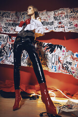 Woman in vinyl black pants and red shoes on art red background