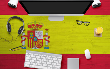 Spain flag background with headphone,computer keyboard and mouse on national office desk table.Top view with copy space.Flat Lay.