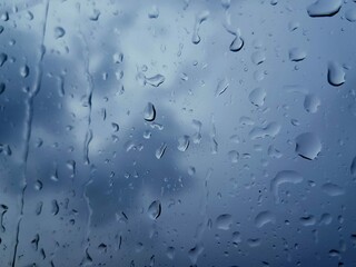 Cloudy sky through glass splashed by rain. The concept of cold rainy autumn. Rain texture background
