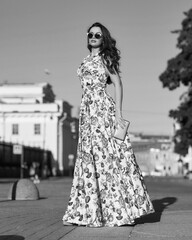 Pretty woman with brunette wavy hair. Full length outdoor portrait. Elegant lady in colorful long sundress at street at sunset. Girl walking in the city. Sunny day.