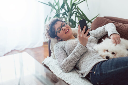 Young Woman Using Mobile Phone. Young Woman Laying On Sofa With Her Dog And Using Mobile Phone.