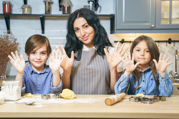 Portrait of a happy family of mom and two children showing hands and smiling while preparing cookie dough in the kitchen