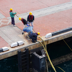 group of people workers in yellow helmets and life jackets moor a cruise ship in the seaport, many...