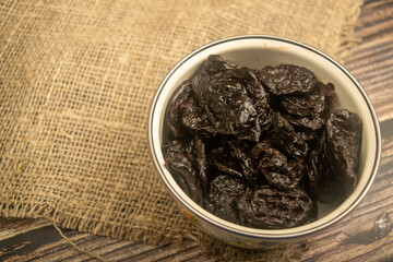 Dried prunes in a metal bowl on a wooden background. Close up.
