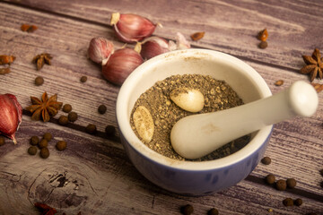 Allspice in a ceramic mortar and scattered garlic cloves, star anise and allspice on a wooden table. Close up.