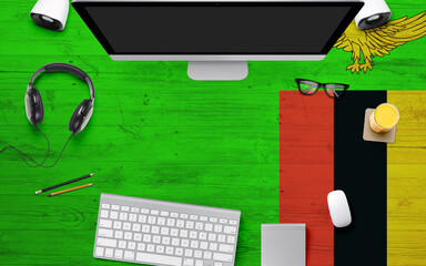 Zambia flag background with headphone,computer keyboard and mouse on national office desk table.Top view with copy space.Flat Lay.