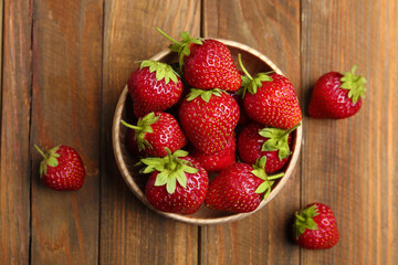 Delicious ripe strawberries in bowl on wooden table, flat lay