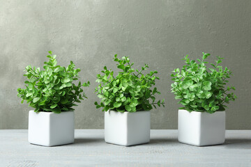Artificial plants in white flower pots on grey wooden table