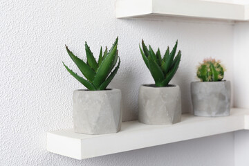 Beautiful artificial plants in flower pots on shelf