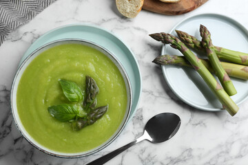 Delicious asparagus soup in bowl on white marble table, flat lay