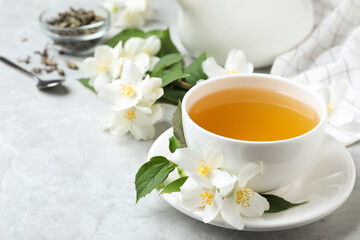 Fototapeta na wymiar Cup of tea and fresh jasmine flowers on light grey marble table