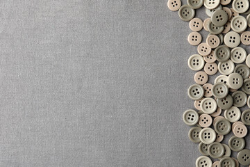 Many plastic sewing buttons on grey fabric, flat lay. Space for text
