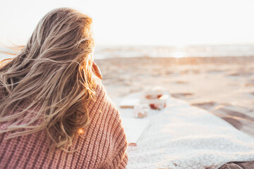 Young blonde woman lying alone on the beach or ocean and look at the horizont. A woman dressed in a warm sweater. Toned. Face is not visible.