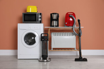 Set of different home appliances with vacuum cleaner near brown wall indoors