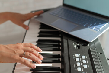 Fototapeta na wymiar Closeup of female hands on an electronic piano. A laptop on a keyboard instrument. Online lesson. Distance learning music.