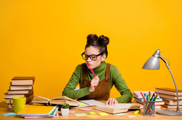 Photo of minded smart girl high school girl sit table prepare exam read book think thoughts what write essay pen touch chin wear green sweater overall isolated bright shine color background