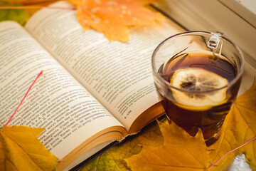 book in autumn yellow leaves with a cup of warm tea with lemon