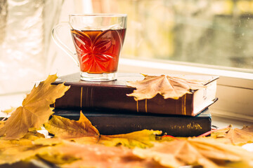 cup of hot tea on books with autumn yellow leaves