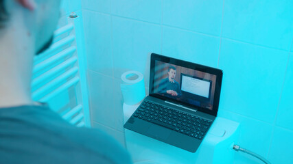 Man watching webinar on laptop computer while taking a leak in toilet