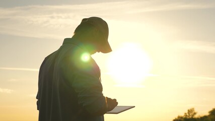 business man working with tablet outdoors. Farmer works with a tablet on a wheat field in the sun. silhouette of an agronomist with tablet studying a wheat crop in a field. - obrazy, fototapety, plakaty