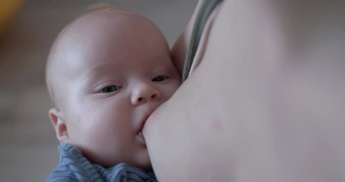 Close portrait of a cute, little baby boy during a breastfeeding at camera