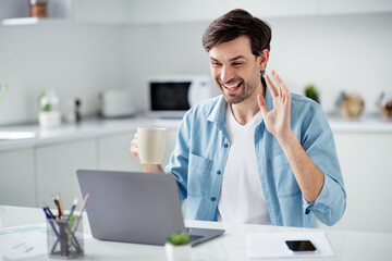 Photo of handsome guy young student browsing notebook sitting table video call online conference friendly talk drink tea good mood say hi miss parents social distance quarantine indoors © deagreez