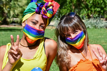 Two pretty women of different race (female friends or lgbt couple) wearing rainbow headdress and...