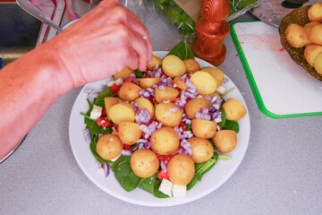 A hand throws salt on a newly- boiled potatoes on a plate with spinach and onions and cheese.