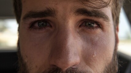 Obraz premium Handsome young man crying looking at camera. Tears run down his cheek. His eyes are bright.