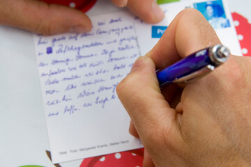 Eine Männerhand schreibt eine Ansichtskarte mit einem Kugelschreiber
