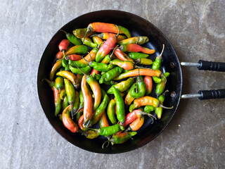 SOME COLORFUL CHILLI PUT IN A PAN ISOLATED ON STONE BACKGROUND