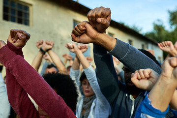 Close-up of crowd of people with clenched fists above head protesting on the streets.