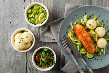 Portion of fried salmon, served with mashed potatoes and cooked leek. Top view. Gray plate, wooden background.