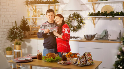 cheerful family couple in Christmas style outfit drinks champagne and hugs showing love in decorated kitchen