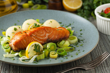 Portion of fried salmon, served with mashed potatoes and cooked leek. Front view. Gray plate, wooden background.