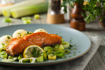 Portion of fried salmon, served with mashed potatoes and cooked leek. Front view. Gray plate, wooden background.