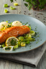 Portion of fried salmon, served with mashed potatoes and cooked leek. Front view. Gray plate, wooden background.